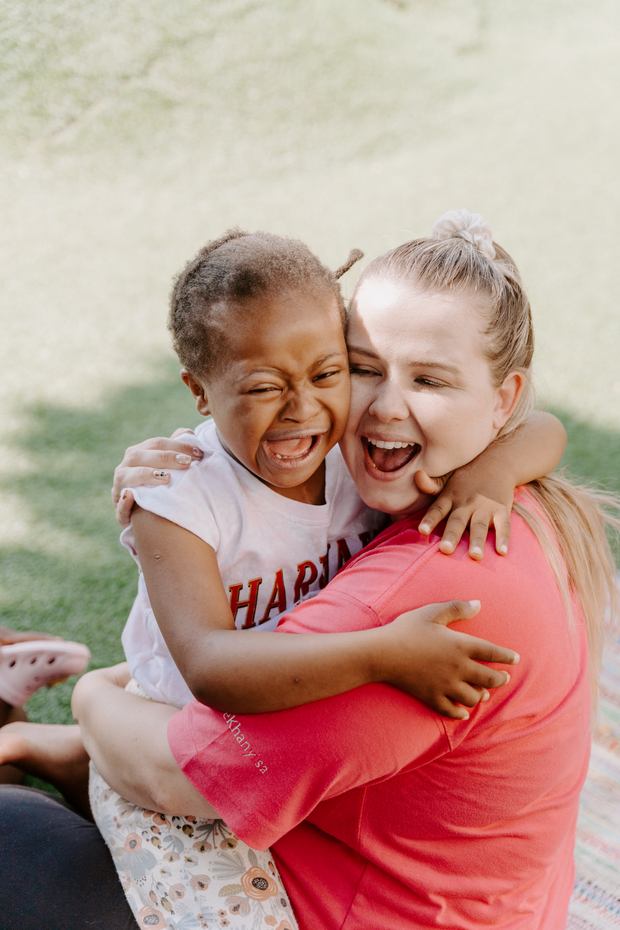 A teacher and a laughing child hugging in the garden at Khanyisa